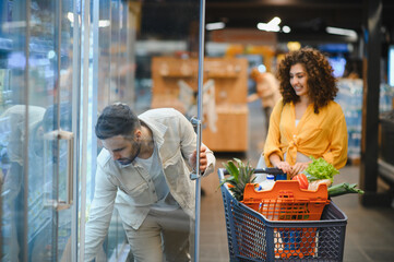 Couple shopping for groceries in supermarket refrigerator aisle