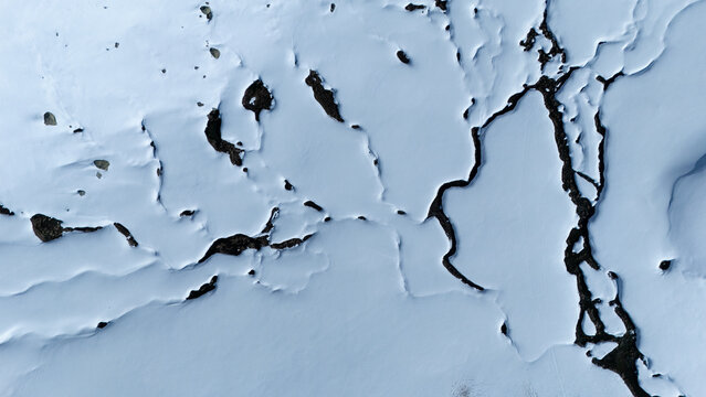 Aerial view of a stark, snow-covered landscape, where the crisp white expanse is dramatically fractured by dark, winding crevices, Wildhaus-Alt Saint Johann, St. Gallen, Switzerland.