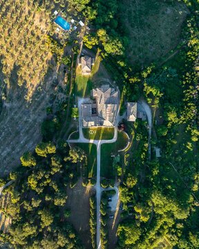 Aerial view of a grand building with a grey tiled roof stands amidst manicured lawns and verdant trees, a swimming pool beckons in the distance, Spoleto, Umbria, Italy.