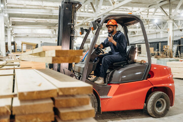 Heavy material, lifting the planks. Warehouse worker operating a forklift while handling wooden materials