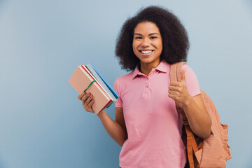 Obraz premium Young African American student smiling holding books and giving thumbs up