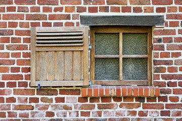 Fototapeta premium Rustic brick wall with an old, weathered wooden window and partially open shutter. Features textured glass, a brick sill, and a sturdy wooden lintel, evoking a classic, timeless architectural feel.
