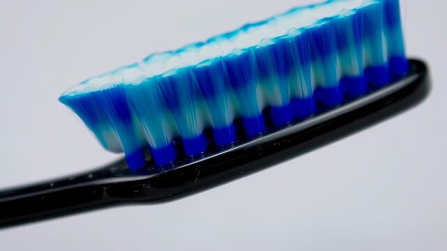 Close-up of a toothbrush head with blue bristles and white paste, held over a white backdrop
