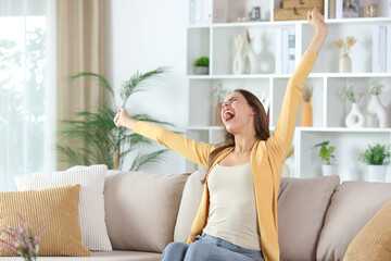 Excited woman in yellow raising arms at home