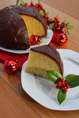 Sliced Italian traditional sweet cake called Parrozzo made with almonds and semolina on a plate on wooden table with Holly branches with red berries and red Christmas glass balls