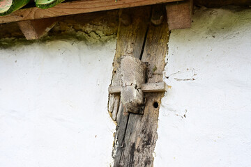 A close-up of a rustic, weathered wooden beam supporting the eaves of a traditional whitewashed farm building. A small, aged wooden latch or fastening mechanism is visible on the ancient post.