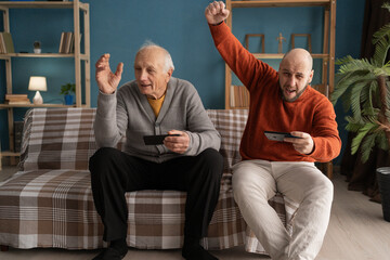 Senior elderly Father and adult son play video games with smartphone and have fun at home spending time together
