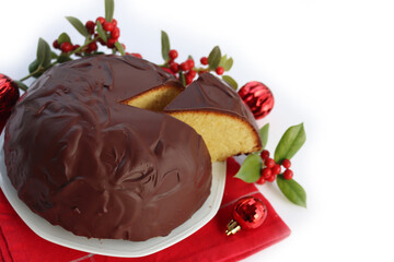 Sliced Italian traditional sweet cake called Parrozzo made with almonds and semolina on a plate isolated on white background with Holly branches with red berries and red Christmas glass balls