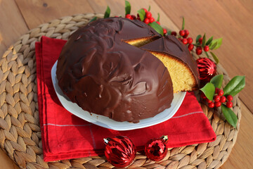 Italian traditional sweet cake called Parrozzo made with almonds and semolina on a plate on wooden table with Holly branches with red berries and red Christmas glass balls