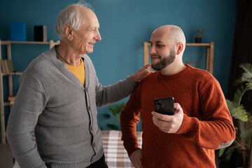 Father's day. Senior man and his son browsing on smartphone in living room.