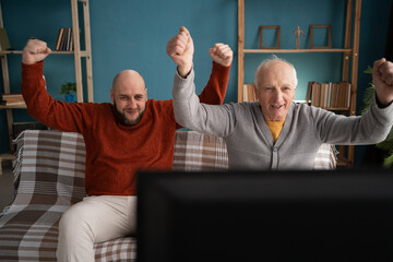 Middle-aged man with his elderly father watching sports at home