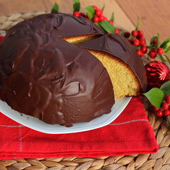 Italian traditional sweet cake called Parrozzo made with almonds and semolina on a plate on wooden table with Holly branches with red berries and red Christmas glass balls