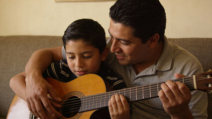 Hispanic father teaching son acoustic guitar at home, warm natural light