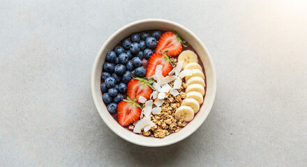 &Auml;sthetische Draufsicht auf eine gesunde Acai-Bowl mit Blaubeeren, Erdbeeren, Banane, Granola und Kokoschips auf minimalistischem grauen Hintergrund &ndash; Konzept f&uuml;r Superfood und veganes Fr&uuml;hst&uuml;ck.
