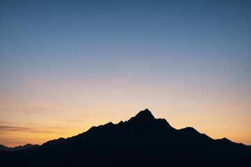 Obraz premium Silhouetted mountain range under soft gradient sunrise sky with wide copyspace and peaceful light for poster, banner, or background use. Ai generative