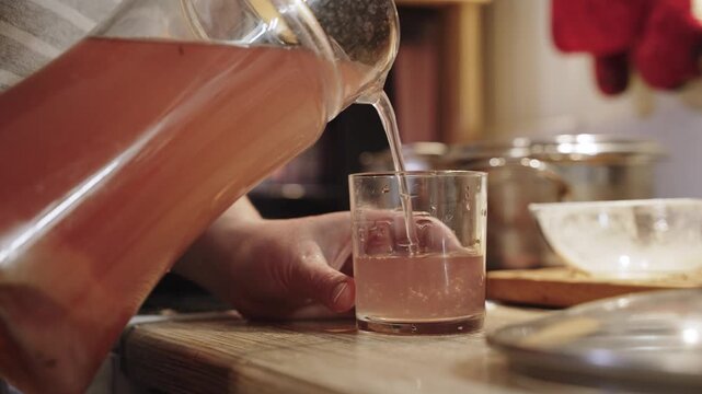 Person pours natural berry compote from pitcher into glass, close-up. Authentic, healthy homemade drink made from fresh berries and fruits with pulp.