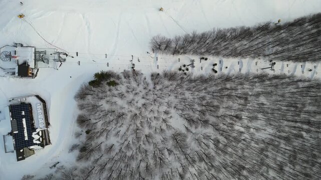 Aerial view of snowy landscape showcasing ski resort and forest, camera smoothly zooms in, revealing intricate details of trees and ski trails, enhancing the winter atmosphere