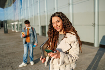 Smiling female student holding a laptop and smartphone on a college campus