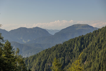 Fototapeta premium vista dettagliata di varie catene montuose ricche di verdi foreste, che si estendono verso l'orizzonte, tra l'Italia e l'Austria, di giorno, con meteo sereno, in estate