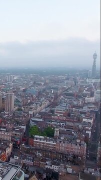 4K aerial vertical video of London skyline featuring the BT Tower in fog. Cinematic drone footage of Fitzrovia rooftops and gloomy city atmosphere. Ideal for travel reels and moody mobile content.