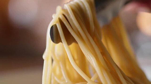 A fork lifts spaghetti with a black olive in a close-up shot