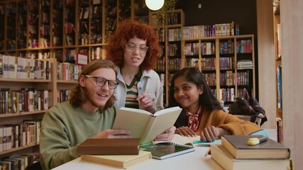 Multi ethnic group of adult students reviewing information in coursebook reading and smiling while collaborating on academic project in library - Powered by Adobe
