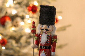 Holiday nutcracker guard standing next to a brightly lit Christmas tree with red ornaments.