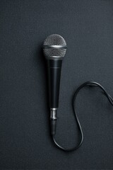 Photo of a black microphone with a long cable, top view, black background.