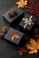 Fototapeta premium A fall-inspired composition of black presents paired with autumn foliage on a deep, shadowy backdrop