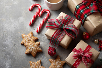 A comforting Christmas composition displays wrapped gifts, plaid ribbon, candy canes, cookies, and star ornaments on a textured gray surface.