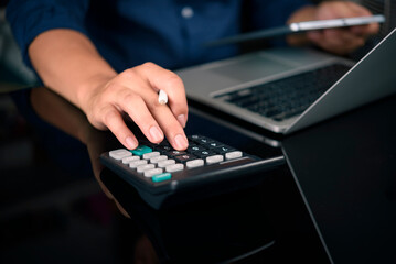 Close up of a professional businessman or accountant hand using a calculator to calculate financial data, tax, cost, and budget while holding a pen and working on a laptop computer.