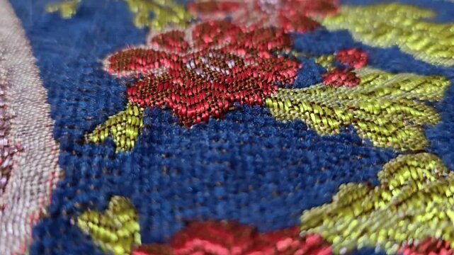 Extreme close up macro shot of luxurious floral embroidery or Jacquard fabric texture in deep blue red and gold moving in slow motion