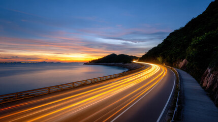 Golden hour coastal road light trail ocean sunset long exposure curve twilight scenic travel. Golden hour coastal road with sweeping light trail beside calm ocean sunset, long exposure curve