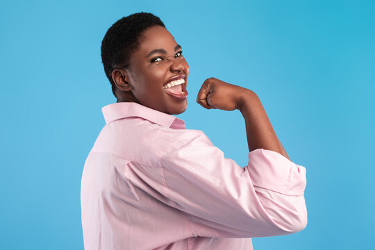 A person with a short black hairstyle smiles joyfully while flexing their arm in a gesture of strength. Bright blue background enhances the feeling of energy and confidence.