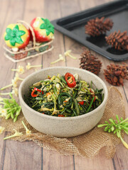 A bowl of tumis pakis dan bunga pepaya—stir-fried vegetable ferns and papaya blossoms—served as a rustic homemade side dish crafted from fresh, seasonal greens. © Tantri