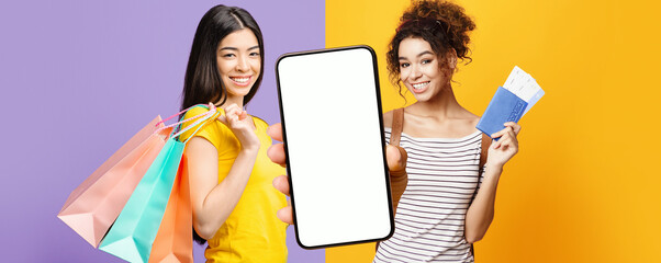 Two young women are smiling while holding shopping bags. One is showing a smartphone while the other holds a wallet. They are on a colorful background of purple and yellow.