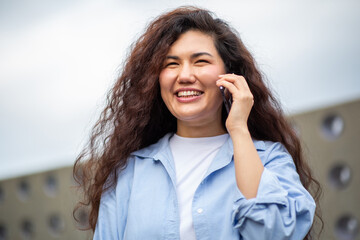 Happy young Asian woman talking on smartphone outdoors in casual denim outfit