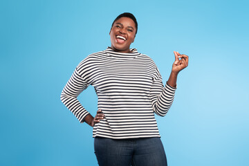 A joyful woman wearing a striped shirt stands with one hand on her hip and the other raised in a...