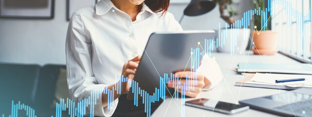 In a bright modern office, a confident European businesswoman engages with clients on her tablet while managing investments. She focuses intently on her financial marketing strategies.