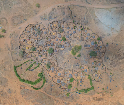 Aerial view of circular Manyatta village with mud huts and thorn fence, blending with the arid landscape, Karamoja, Northern Region, Uganda.