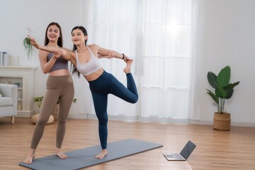 Obraz premium Two women practice yoga together in a bright indoor space with a laptop nearby for guidance in the morning hours