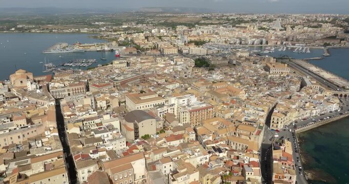 Aerial view of the island of Ortigia, in the historic centre of Syracuse, Sicily, Italy. It overlooks the sea. In the background is the city's marina and the new town. It is a sunny summer morning.