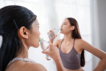 Two women drinking water while wearing workout clothes in a bright indoor space during a fitness break