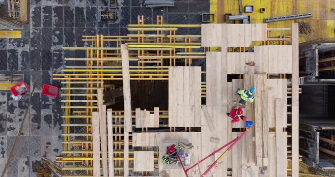 Direct aerial shot of construction workers assembling formwork on modern building site. Scene highlights teamwork, construction industry, and occupational safety in Poland and the EU.
