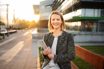 Businesswoman smiling holding tablet in urban sunset at modern office