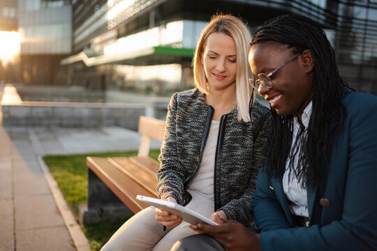 Diverse businesswomen collaborating outdoors using digital tablet - Powered by Adobe