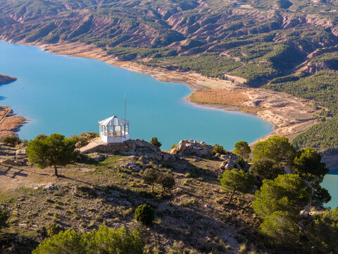 Aerial view of the white caseta guarda standing proudly atop the hill overlooking the turquoise lake against the backdrop of rugged terrain, Vista Caseta Guarda, Andalusia, Spain.