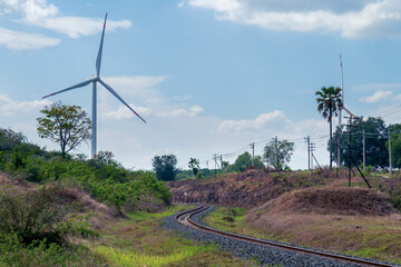 Wind turbines and railway tracks against a daytime sky and clouds. Green energy, electricity generation, and transportation concept.