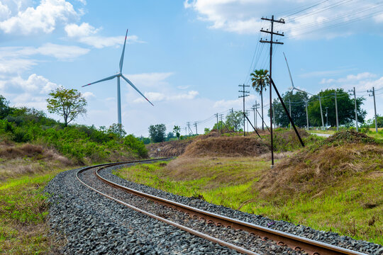 Wind turbines and railway tracks against a daytime sky and clouds. Green energy, electricity generation, and transportation concept. - Powered by Adobe
