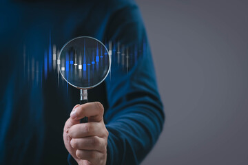 Hand holding magnifying glass analyzing digital candlestick chart, representing financial analysis, data review, investment research, market trends, and modern trading insights.